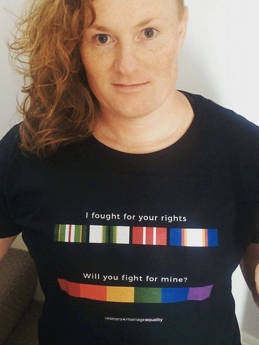 Transgender activist in a protest t-shirt. Head shorn on one side, shoulder-length hair on the other.