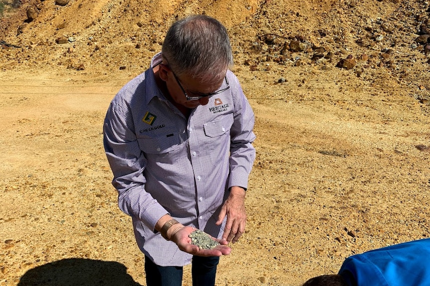 A man with glasses in a blue shirt holds a handful of dirt.