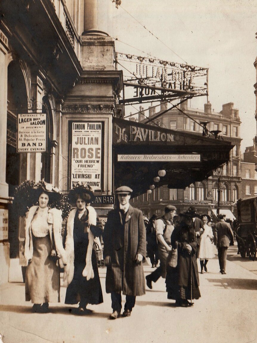 People dressed in clothes from the early 20th Century walk past a theatre called The Pavilion with signs for Julian Rose.