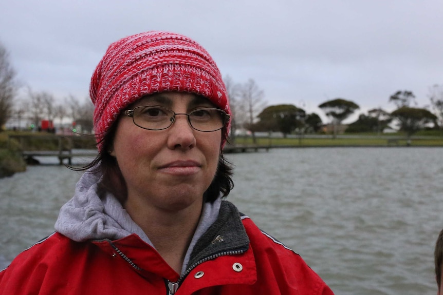 Janelle Cook stands with a red beanie on her head in front of the lake at Caroline Springs on a cold day.