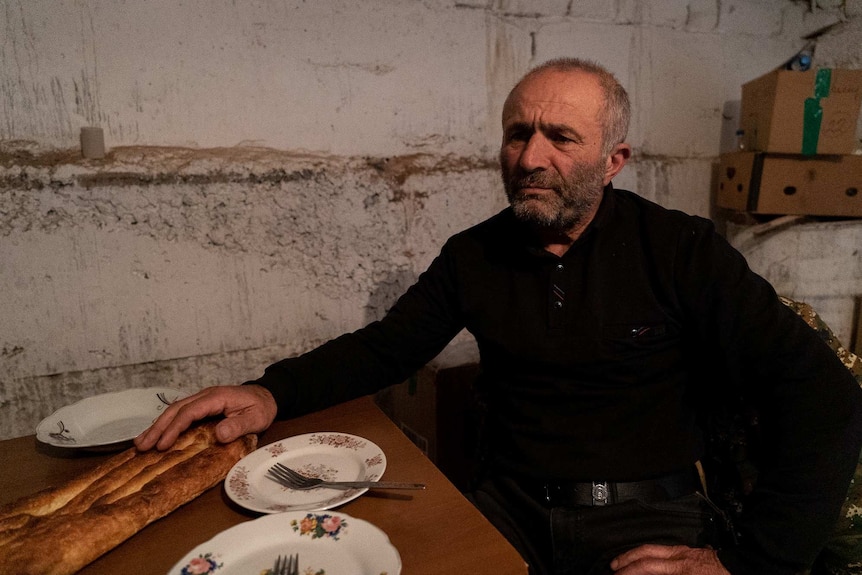 A man with a distressed face sits at a table with empty plates and a baguette