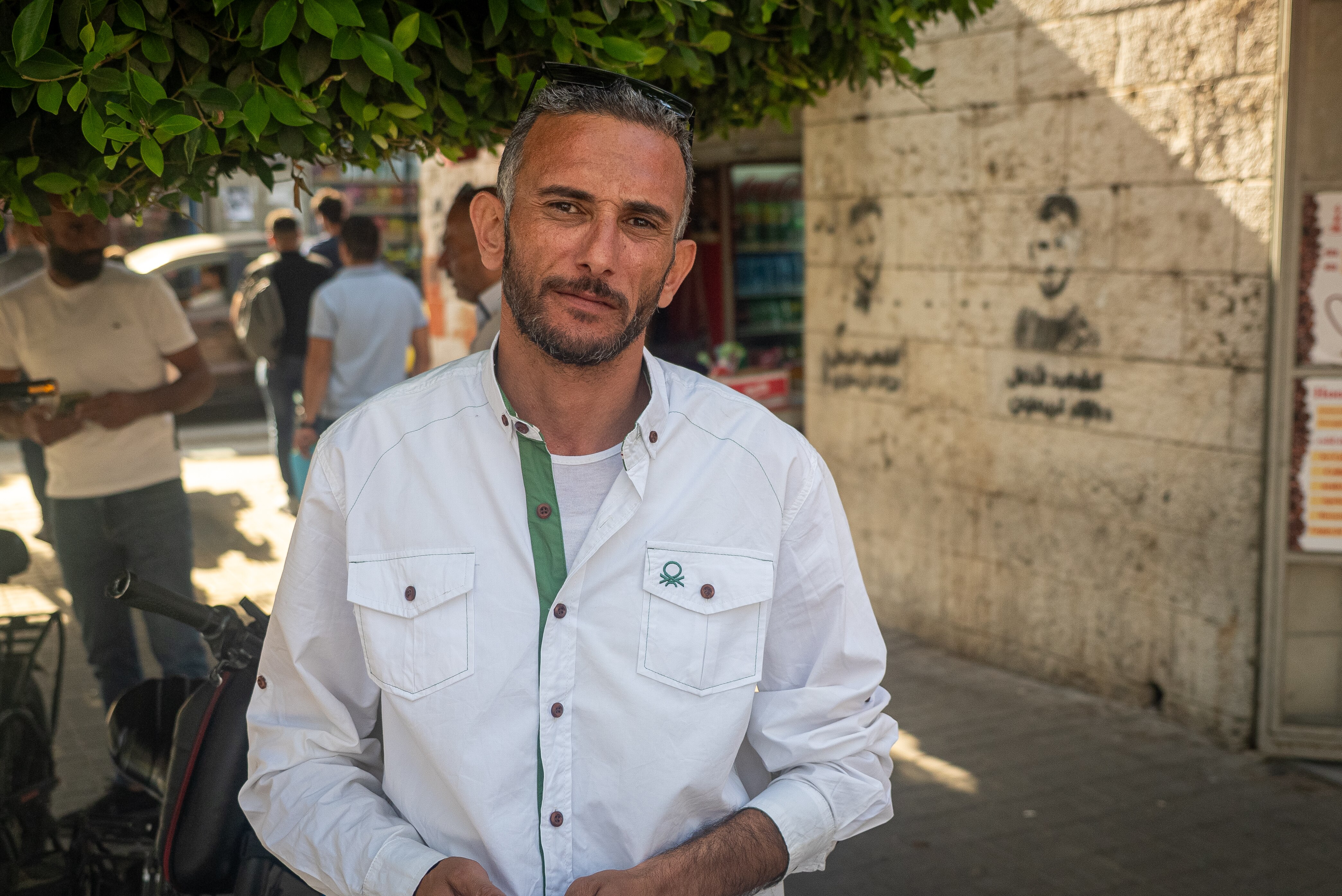A man stands in the shade of a tree in a town square.