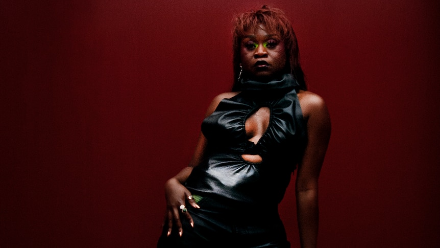 Sampa The Great wearing eye makeup and a black dress in front of a dark red background