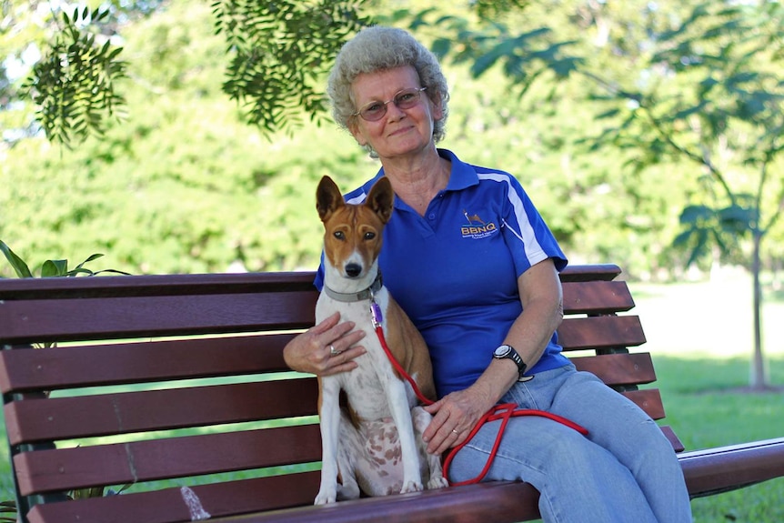 a woman sits on a park bench with a basenji dog