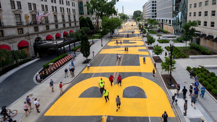 A view from above of a huge Black Lives Matter mural painted in bright yellow letters on a wide street