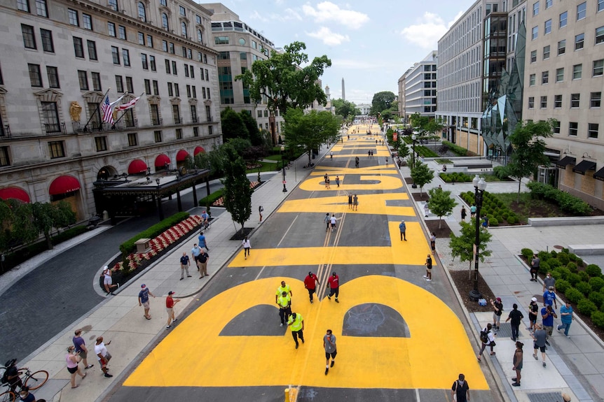 A view from above of a huge Black Lives Matter mural painted in bright yellow letters on a wide street