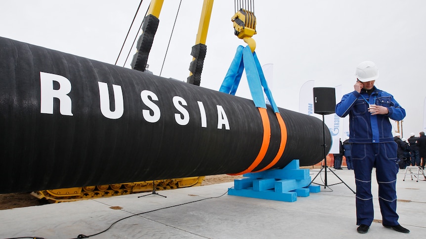 A construction worker speaks on a mobile phone in front of a pipe that reads 'Russia'