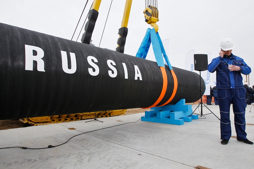 A construction worker speaks on a mobile phone in front of a pipe that reads 'Russia'