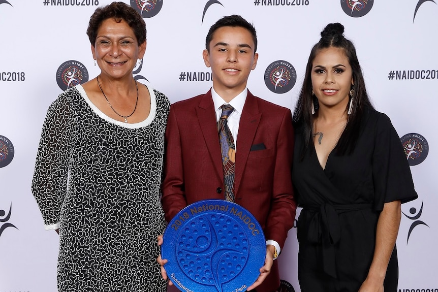 Jack Peris at the 2018 Naidoc awards, holding his award, standing between two women