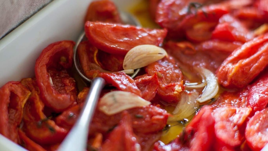 A spoon sits in a white dish filled with confit tomatoes.