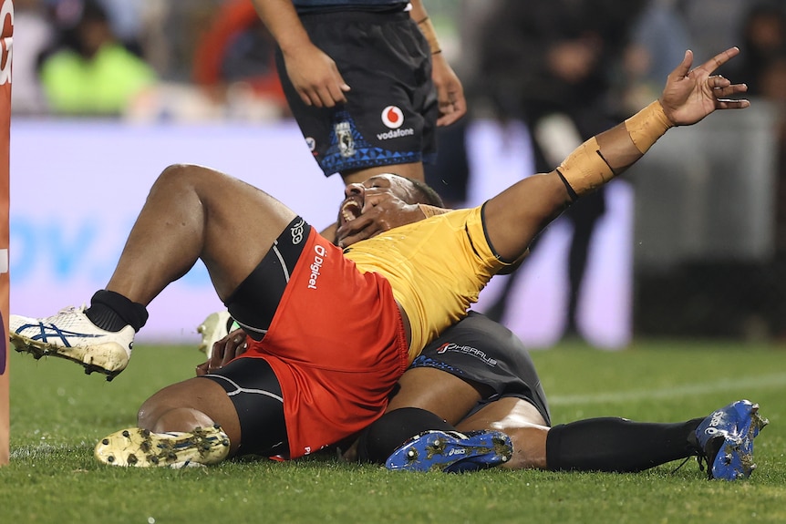 McKenzie Yei celebrates a try for Papua New Guinea while a Fiji tackler lies under him.