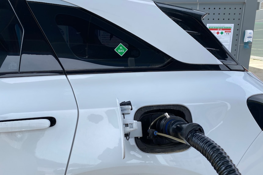 A close up of a white car being refuelled.