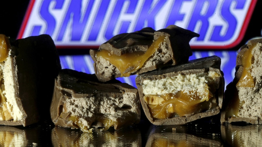 A pile of snickers bars cut in the middle with a packaged Snickers in the background. 