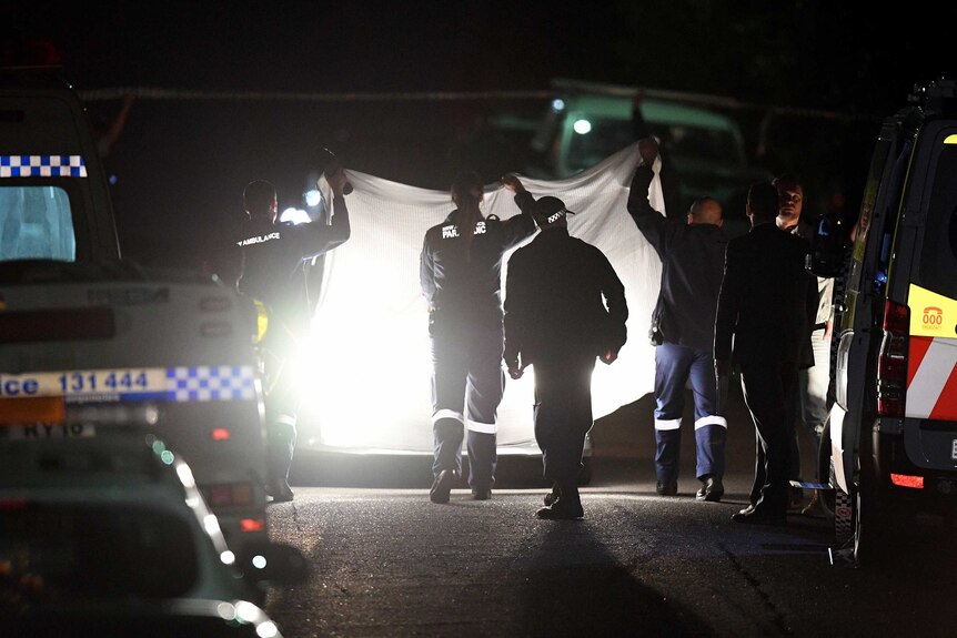 Police and emergency services at the scene of a shooting, holding up a white sheet.