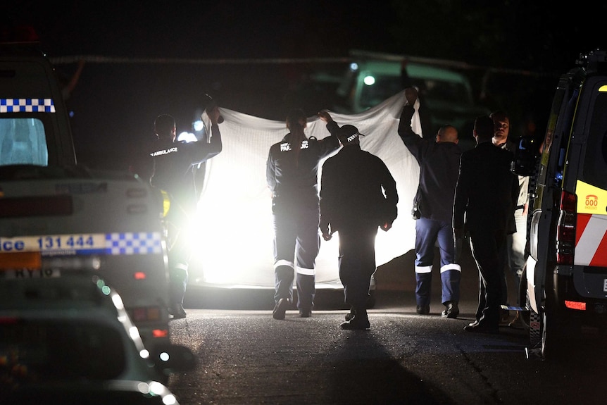 Police and emergency services at the scene of a shooting, holding up a white sheet.