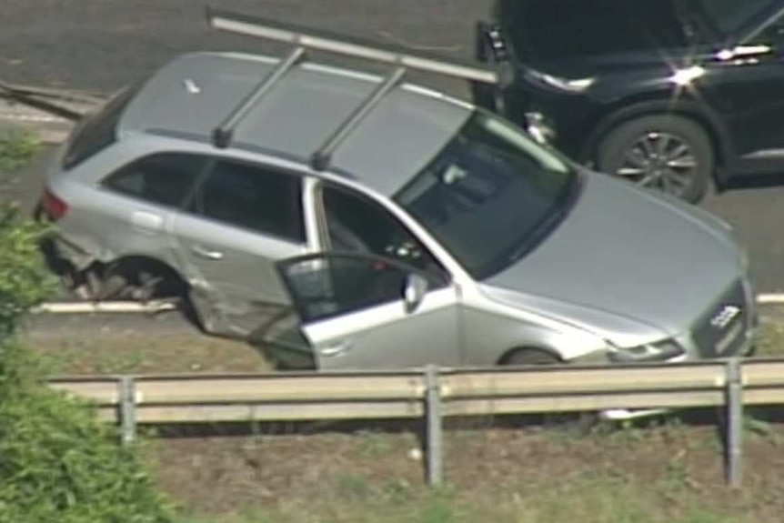 A silver car is crashed at the side of a highway.