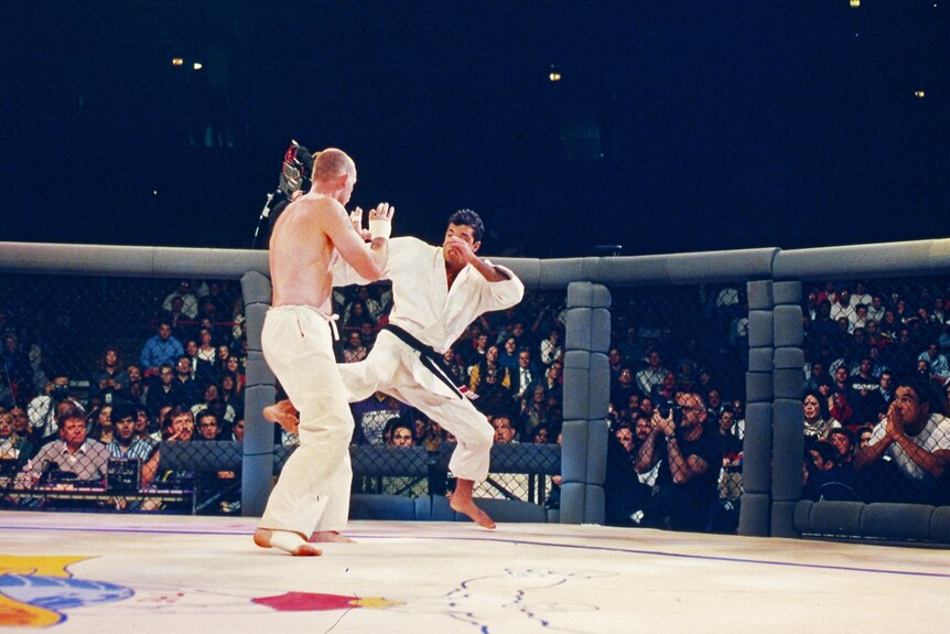 Royce Gracie, in a black and white gi, tries to kick Gerard Gordeau, in long white pants, during UFC 1.