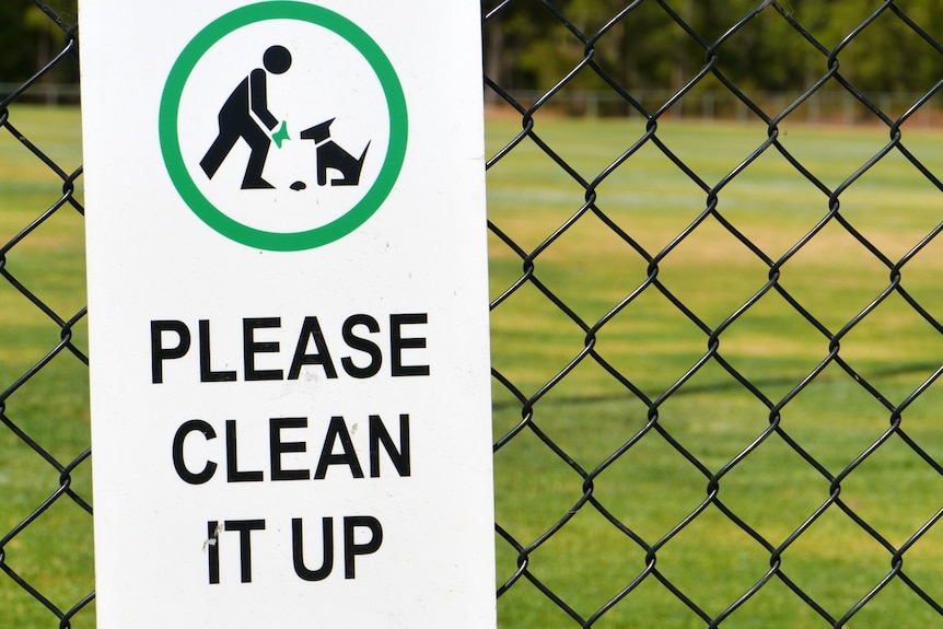 A sign on a fence urging people to clean up after their dogs.