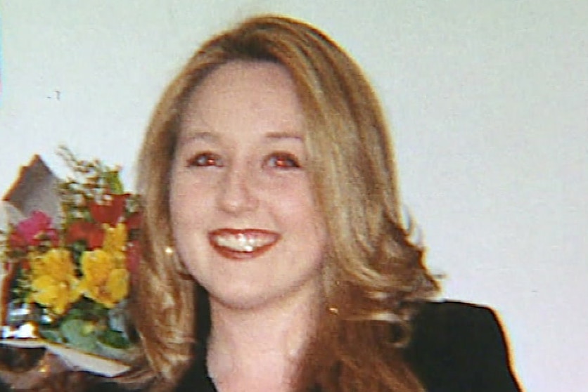 A headshot of a smiling Sarah Spiers wearing a black jacket in a room with flowers in the background.