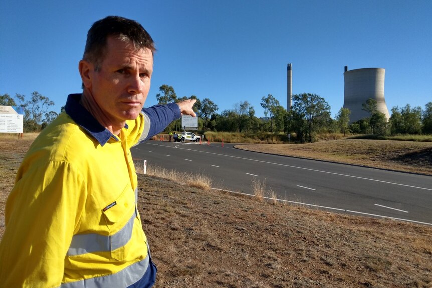 A man in a high vis work shirt points to a power station. 