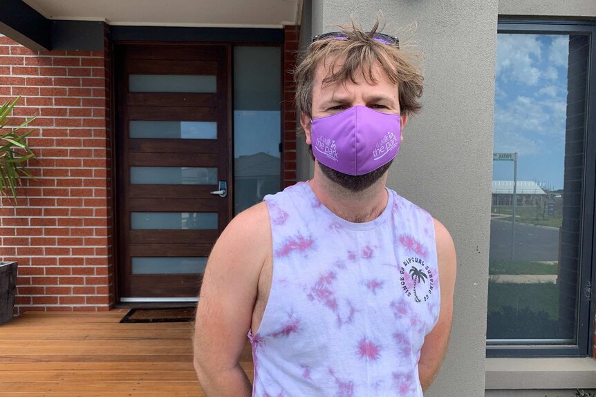 A man in a singlet and purple face mask looks at the camera.