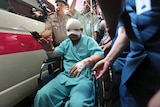 A man sits in a wheelchair as he leaves the general hospital, his head wrapped up in bandages.