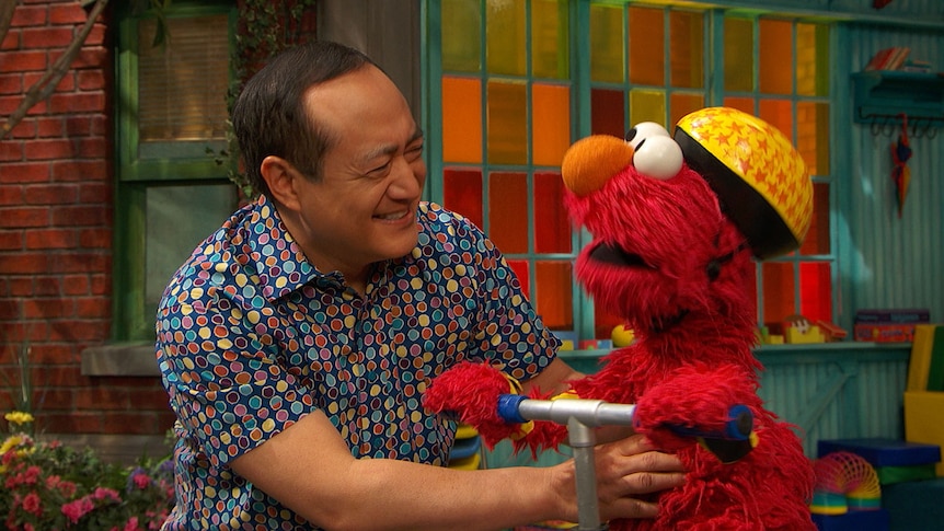 Elmo, wearing a helmet holding a pogo stick, with Alan