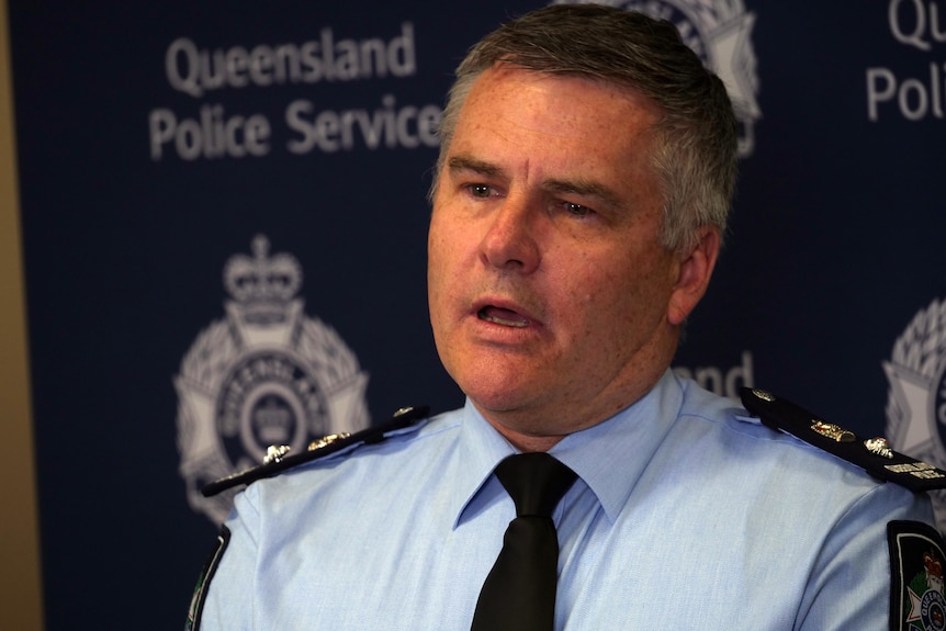 A grey-haired policeman speaks in front of a branded backdrop.