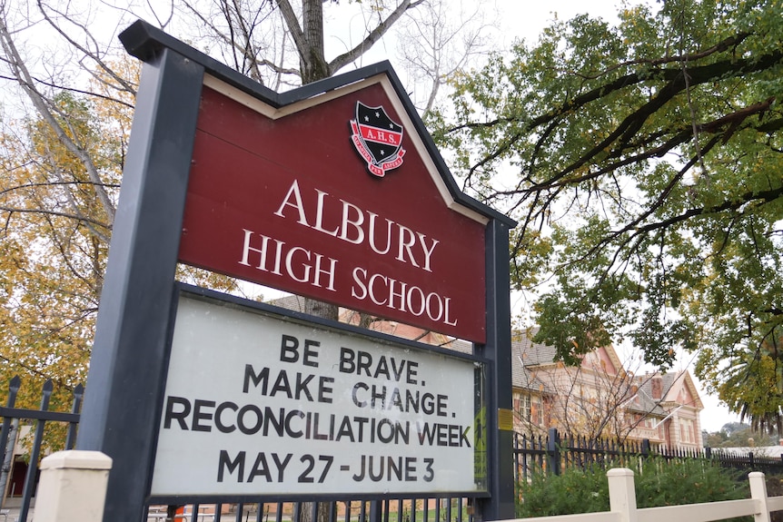 A maroon sign outside a big brick building that says Albury High School