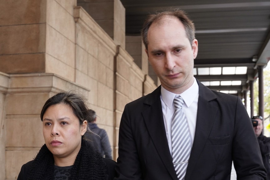 A woman and man both wearing dark coloured clothing walk outside a court building