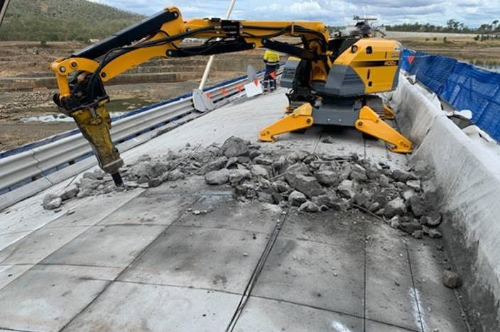 A yellow digger drills into the top of Paradise Dam's spillway as part of essential works.