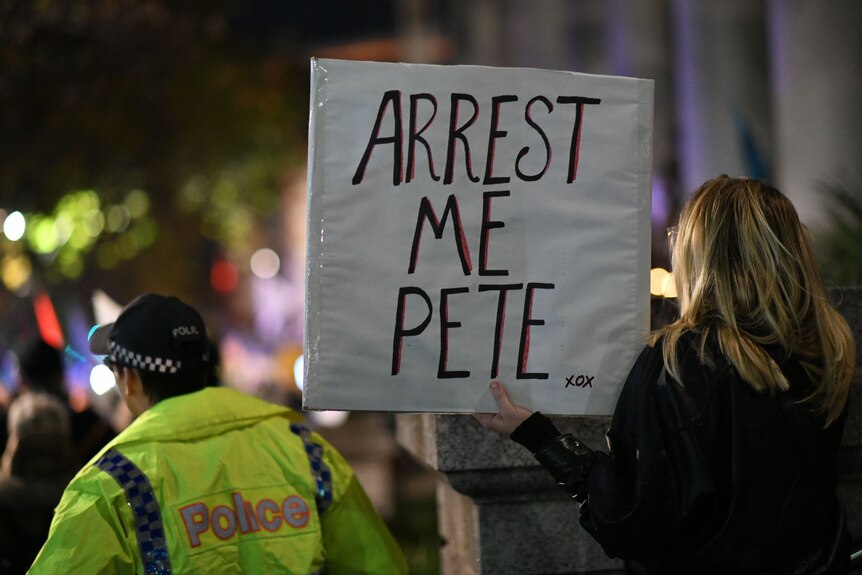 A woman holds a sign which reads 'arrest me pete' 