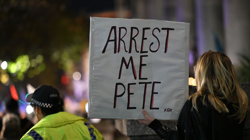A woman holds a sign which reads 'arrest me pete' 