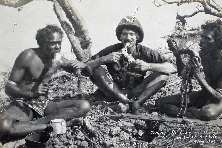 A non-Indigenous man eats a fireside meal with Aboriginal men. 