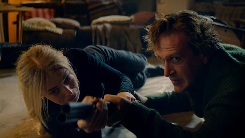 A man and a woman lie on the floor of a house fighting over a gun.