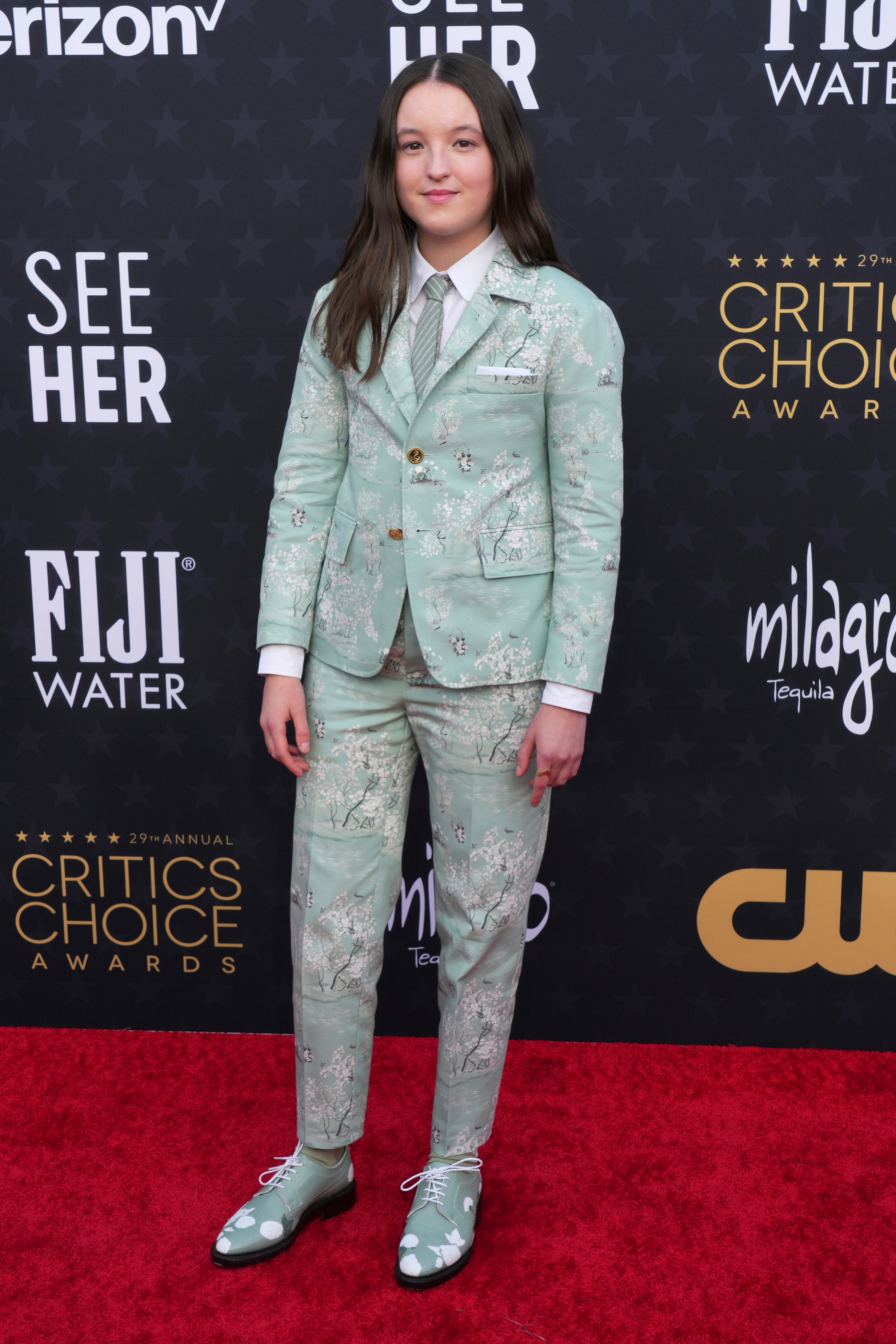 Bella Ramsey wearing a mint green floral suit with matching green shoes.