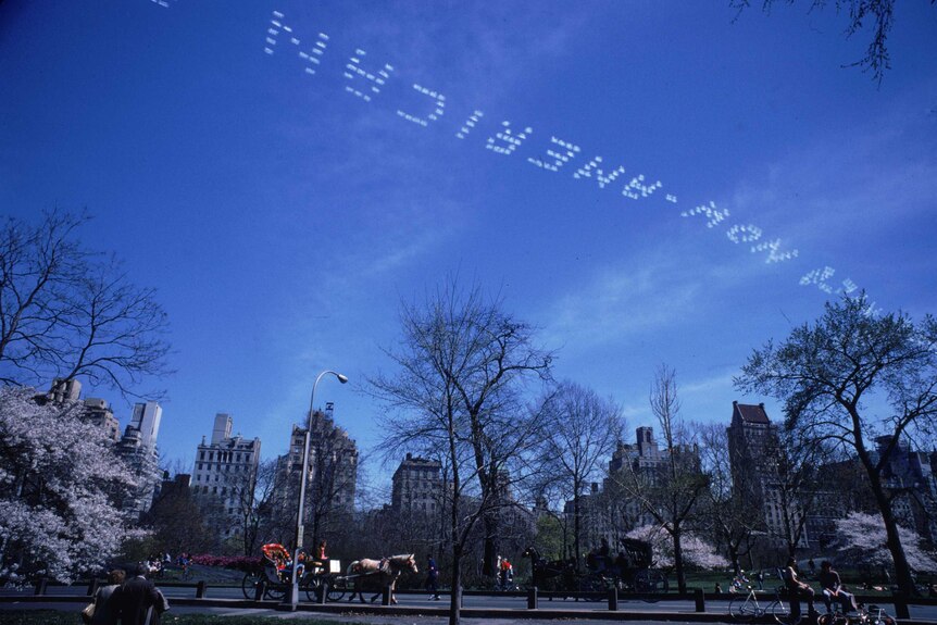 A skywriter trails a message across the sky over New York's Central Park, using the smoke trails of his aircraft to form words.