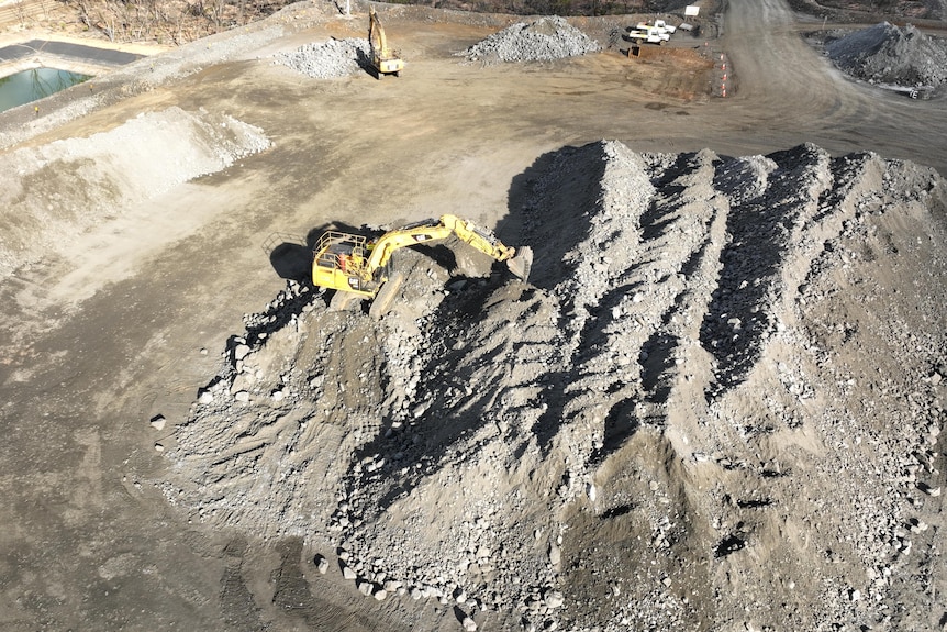 An aerial image of IGO's Nova mine showing a large pile of rocks and dirt with a yellow digger moving rocks.