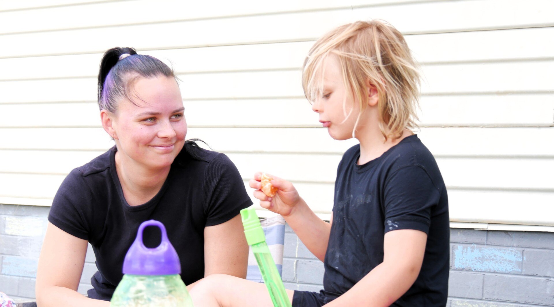 A woman and a young boy sit outside a home.
