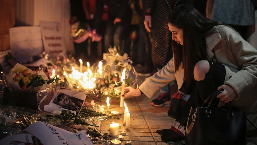 a woman kneels to light a candle with people behind her