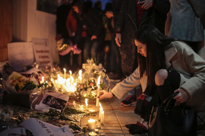 a woman kneels to light a candle with people behind her