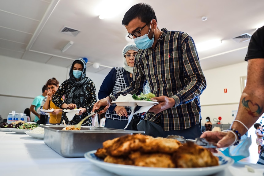 people in masks lining up and taking food from a table