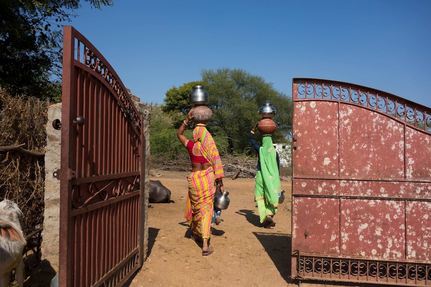 Women in bright clothes carry water jugs on their heads