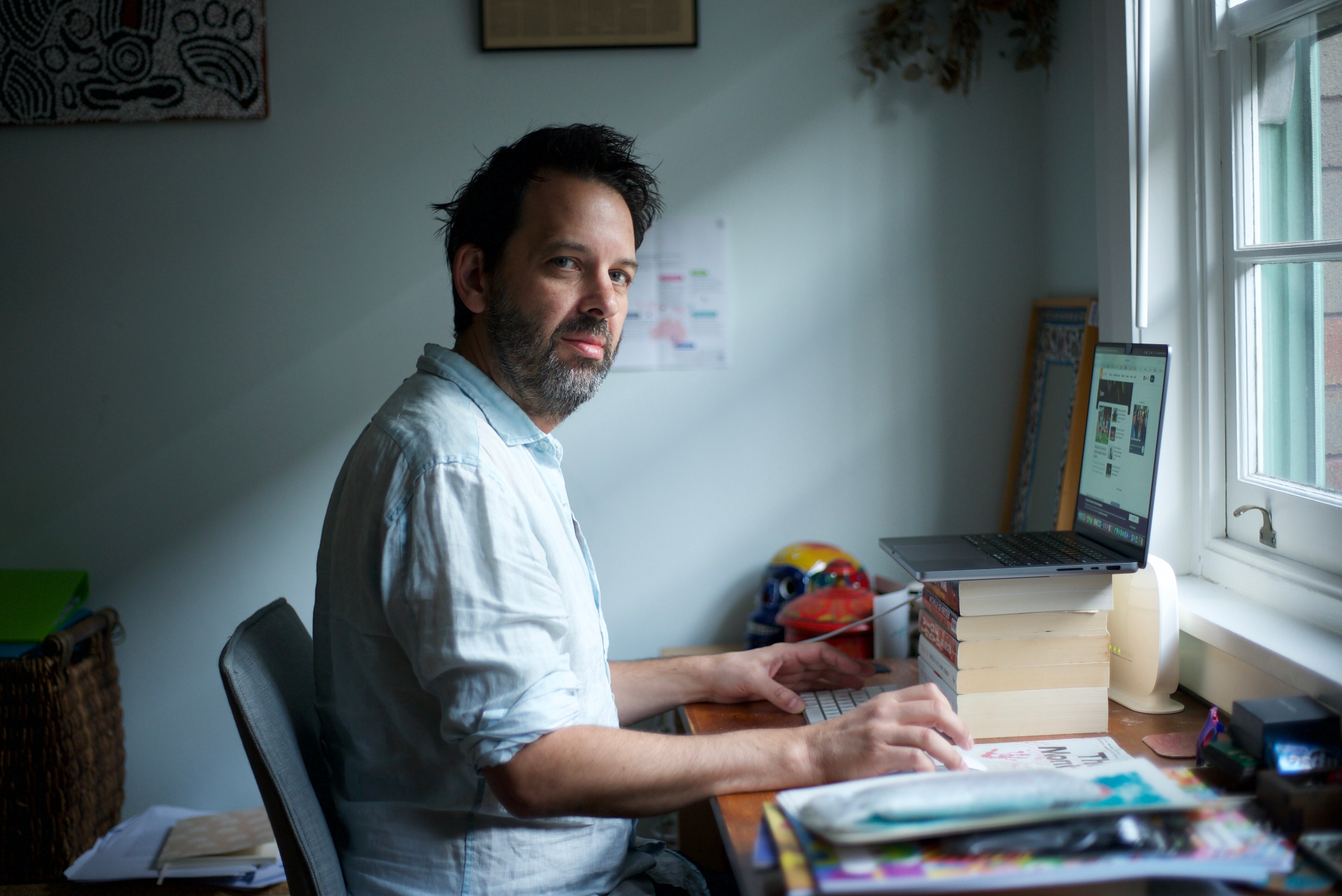 Antony Loewenstein sits at his desk by his computer and looks at the camera 