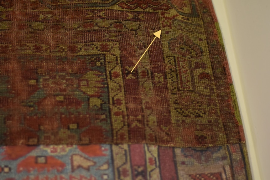 Close up image of a carpet with a yellow arrow pointing to Islamic script.