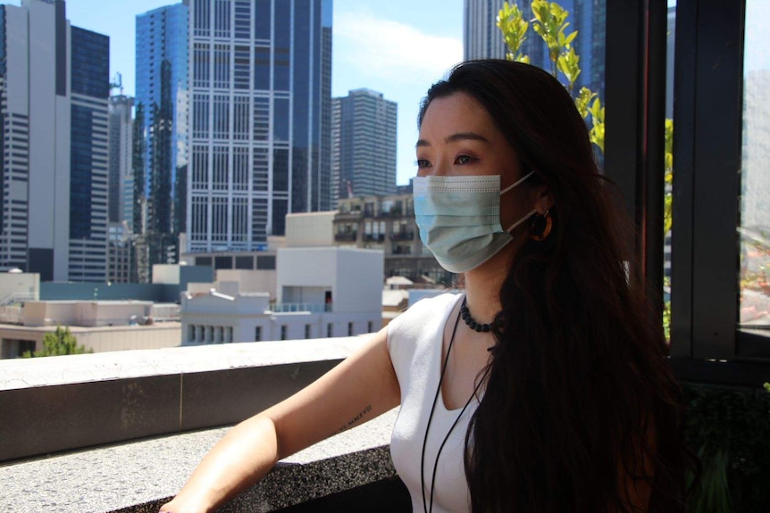Tiffy Sze stands on her bar's balcony in front of a Melbourne city backdrop.