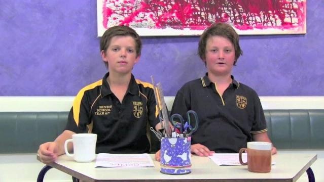 Two teenage boys sit behind desk