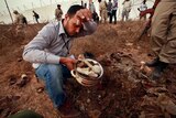 A man collects human remains at the site of a mass grave in Tripoli