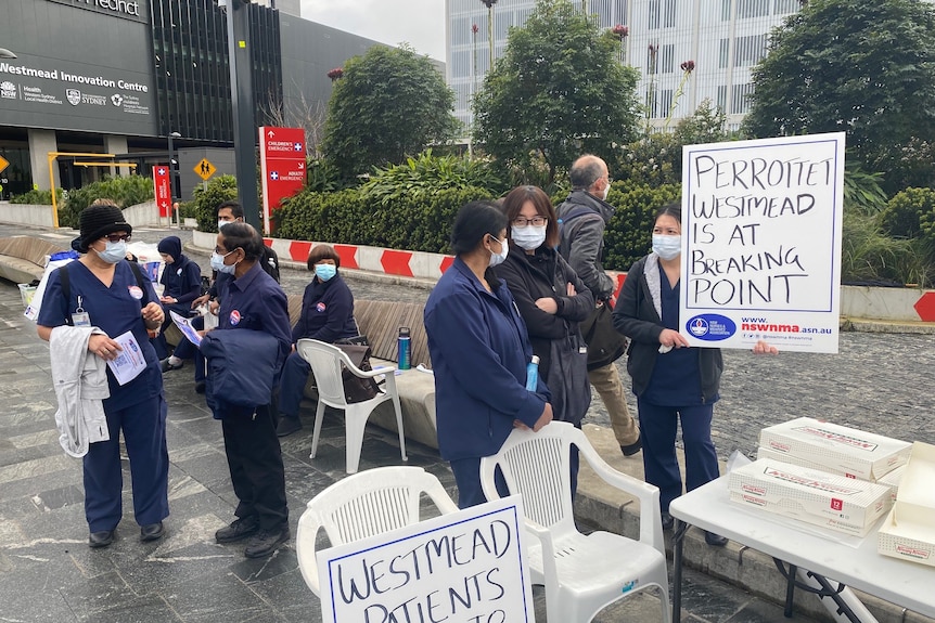 Nurses in their uniforms gather outside a hospital with a sign saying "Perrottet Westmead is at breaking point"