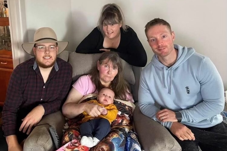 A woman sitting holding a baby surrounded by three adults.